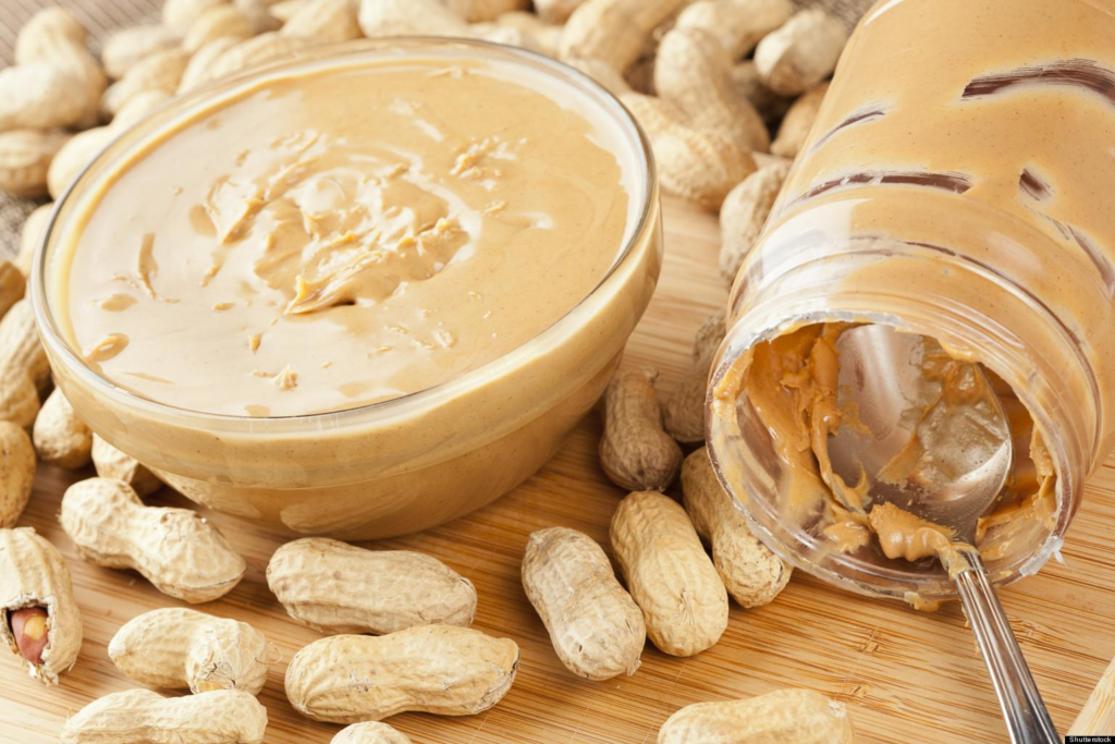 Homemade peanut butter in a glass jar with peanuts around