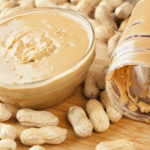 Homemade peanut butter in a glass jar with peanuts around